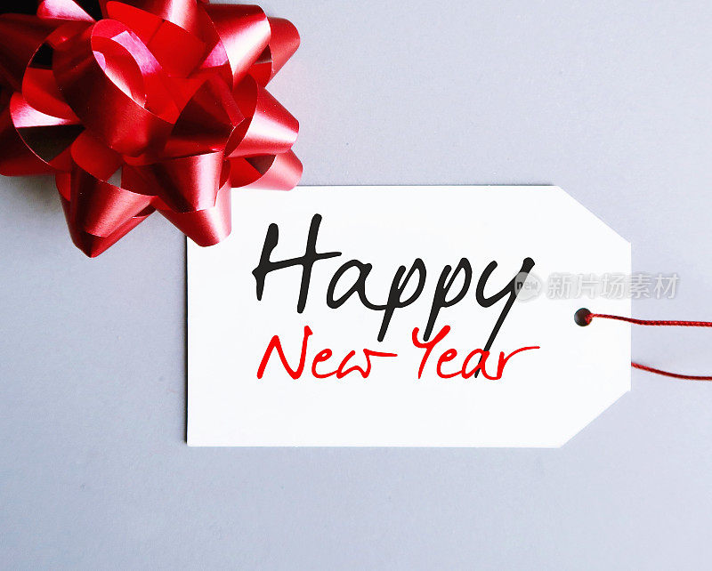 红色的礼物蝴蝶结和白色的礼物吊牌，手写文字HAPPY NEW YEAR新年概念节日贺卡，节日送礼，给大家温馨的祝福